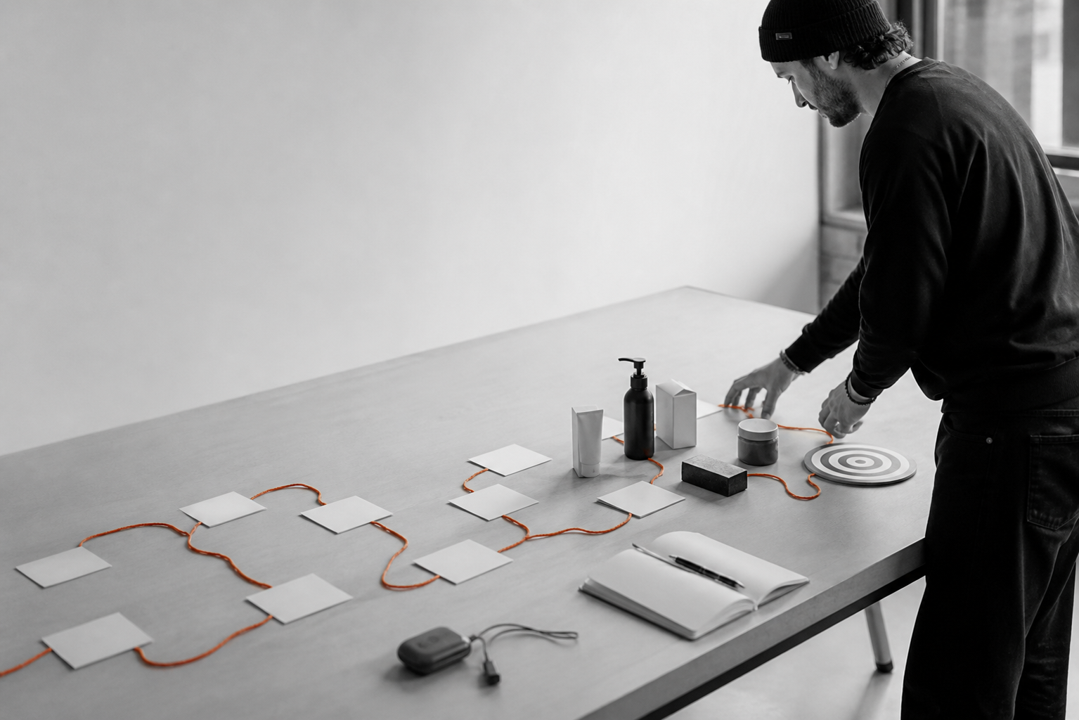 Un homme relie des cartes et divers objets par un cordon orange sur une table